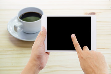 hands of a man holding blank tablet device over a wooden workspace with coffee on table