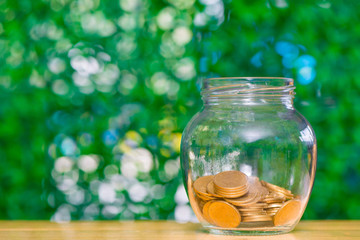 Gold coin money in the glass jar on table in garden with green background, for saving banking financial concept.