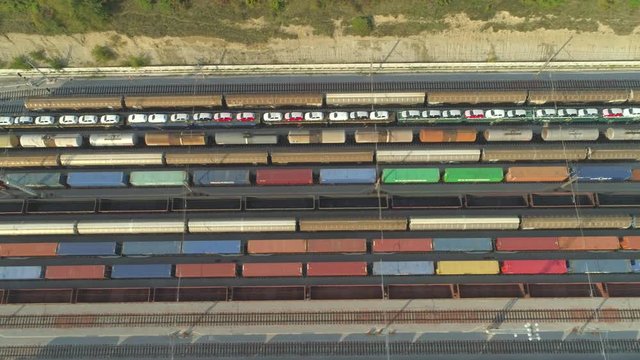 AERIAL TOP DOWN: Flying above industrial railroad station with cargo trains and freight containers on sunny day. Fully loaded railroads and shipping container trains on industrial railway terminal.