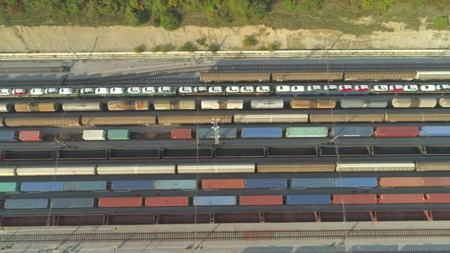 AERIAL TOP DOWN: Flying above loaded cargo train leaving industrial railroad station with freight containers on sunny day. Heavy railroads and shipping container trains on industrial railway terminal.