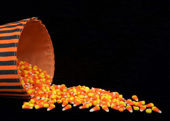 Candy corn traditional to Halloween spilling out of a black and orange bucket onto a black background with copy space - Powered by Adobe