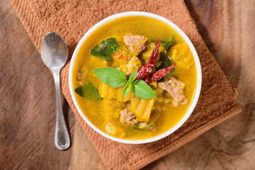 Thai food.Spicy pumpkin soup with pork in a bowl on brown fabric and wooden background.Top view of food