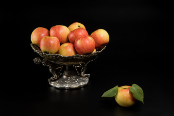 apples with leaves in a vase on a black background