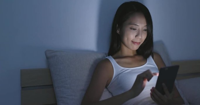 Woman use of cellphone on bed at night