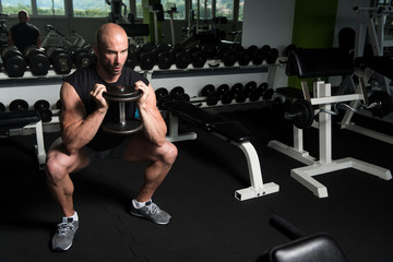 Fototapeta na wymiar Muscular Man Exercising Quadriceps With Dumbbells