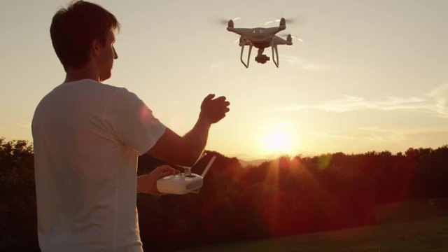 SLOW MOTION CLOSE UP LENS FLARE Young man hand landing quadro drone with modern white RC transmitter. Male filmer controlling drone over RC radio controller. Man flying and filming with drone camera