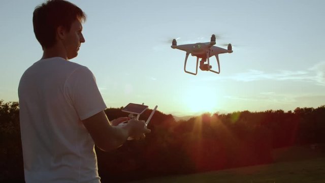 SLOW MOTION CLOSE UP LENS FLARE Young man hand launching quadro drone with modern white RC transmitter. Male filmer controlling drone over RC radio controller. Man flying and filming with drone camera