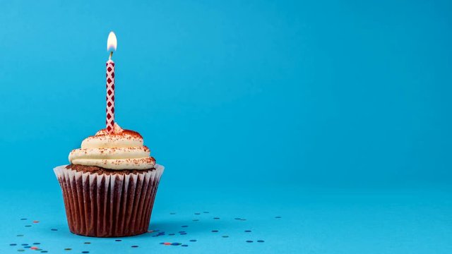Cupcake birthday party with candle and confetti cinemagraph on blue background seamless loop. 