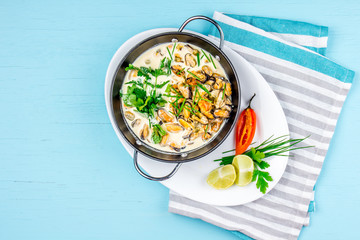 Mussels in creamy milk sauce with aromatic herbs and lemon. Top view Blue background. Top view