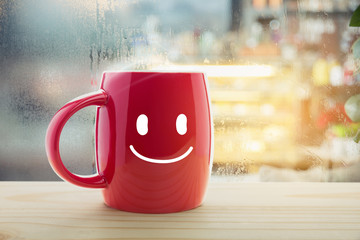 Red mug of coffee with a happy smile, Steaming red coffee cup on a rainy day window background, Good morning or have a happy day message concept
