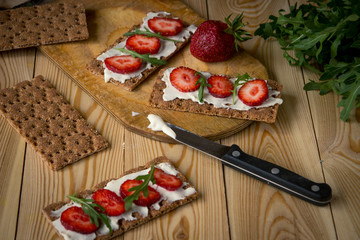 Wholegrain rye crispbread crackers with cream cheese, strawberry and arugula