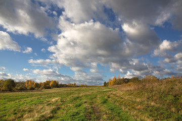 Fototapeta premium Colorful autumn landscape with a field in hilly terrain. Evening. The sky with heavy white clouds. Picture, Wallpapers, calendar.