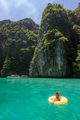 Lady with red hat on yellow pool float chic in beautiful crystal clear water at Pileh bay at Phi...