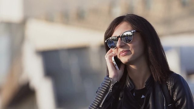 Stylish business woman wearing sunglasses at the sunset gladly talks over the phone