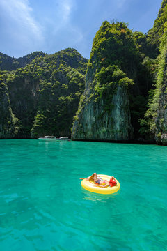 Lady with red hat on yellow pool float chic in beautiful crystal clear water at Pileh bay at Phi Phi island near Phuket, Thailand