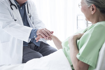 A geriatric doctor gently holding a hand of a female patient