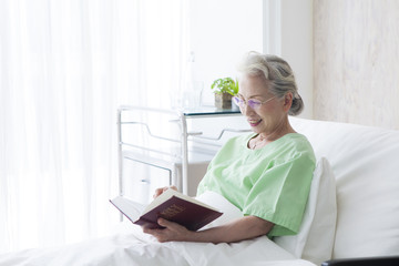 An old female patient is reading the Bible in a hospital room