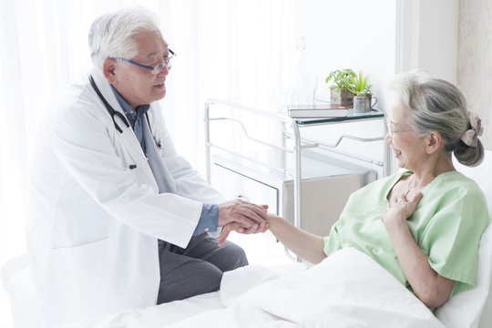 A geriatric doctor gently holding a hand of a female patient with a smile