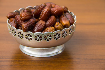 Dates fruit on a silver bowl on wooden table. The Muslim feast of the holy month of Ramadan Kareem