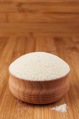 Semolina in wooden bowl on brown bamboo board, closeup. Healthy dietary groats  background.