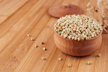 Green buckwheat in wooden bowl on brown bamboo board, close up. Rustic style, healthy dietary groats  background.