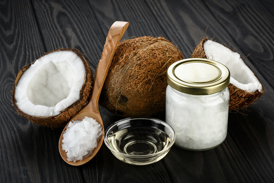 Coconut, glass jar and wooden spoon with coconut oil on a wooden background.