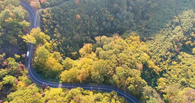 Aerial drone view of a curved road through the autumn forest with van