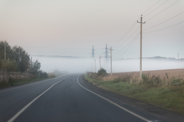 The road in the fog. Electric poles near the road in the morning.