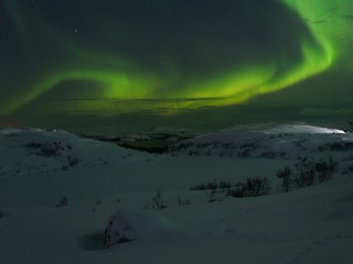 Hills and tundra covered with snow and in the sky the stars, the Aurora.
