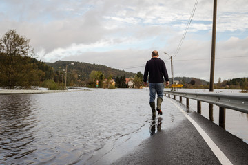Man walking on the flooded road, water comes from the river Tovdalselva in Drangsholt in Kristiansand, Norway - October 3, 2017.