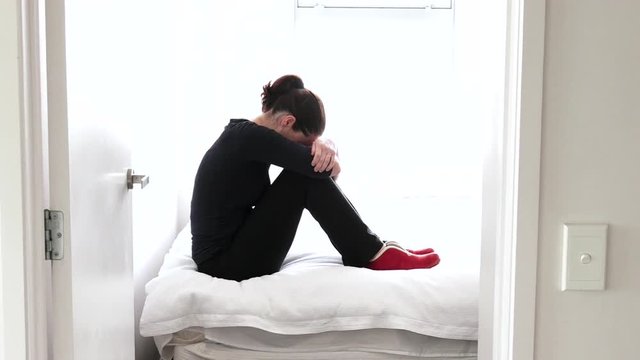 Depressed adult victim woman (age 30-40) sitting and crying on the bed at home, suffering from a severe depression. Victim concept photo of hijack, rape and crime