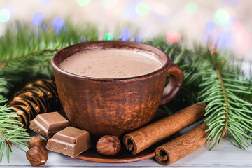 Lumières de Noël floues, tasse de chocolat chaud au lait, cubes de chocolat cassés, bâtons de noisette et de cannelle, branches d& 39 arbre de Noël, pomme de pin sur des planches de bois blanches