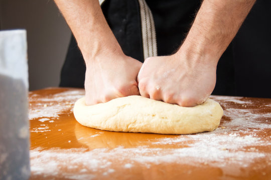 Male baker kneading dough on flour covered table