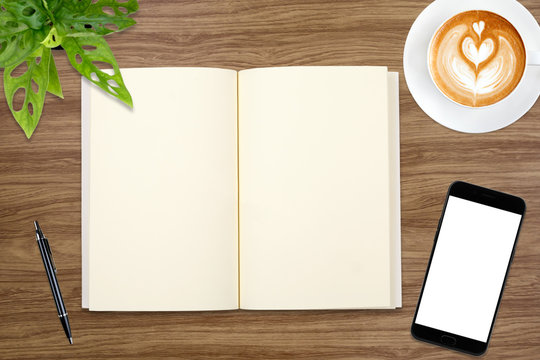 An open blank notebook, smartphone with pen and a cup of latte coffee on wooden table.