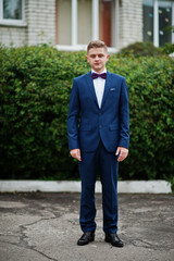 Portrait of a fashionable and stylish high school graduate in elegant tuxedo posing outdoor with bushes on the background. © AS Photo Family