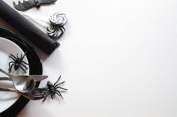 Halloween table setting accessories: black service plate, white salad plate, silver cutlery and napkin with horror candies  and decorative spiders and bat. Happy Halloween party concept. Copy space.