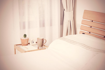 White pillows and bedding in blue bedroom interior in morning time with alarm clock on wooden bed side table