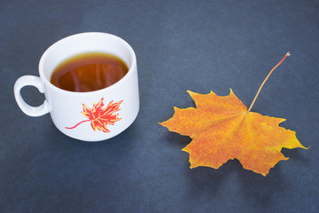 Autumn composition, colorful leaf and a cup of hot tea on the black background.