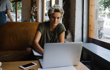 Blonde girl is reading emails on a screen of a modern portable computer while sitting in a cafe....