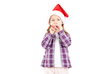 Portrait of sweet little girl in Santa hat blowing into party blower