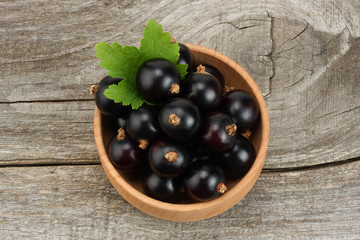 black currant in wooden bowl with green leaf on old wooden background. top view