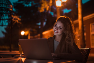 Beautiful girl working at night on a laptop, outdoors. High ISO image.