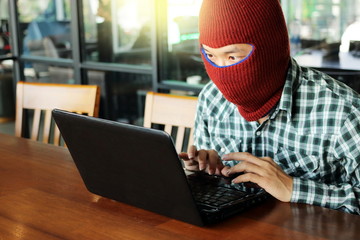 Masked hacker wearing a balaclava stealing data from laptop. Internet crime concept.