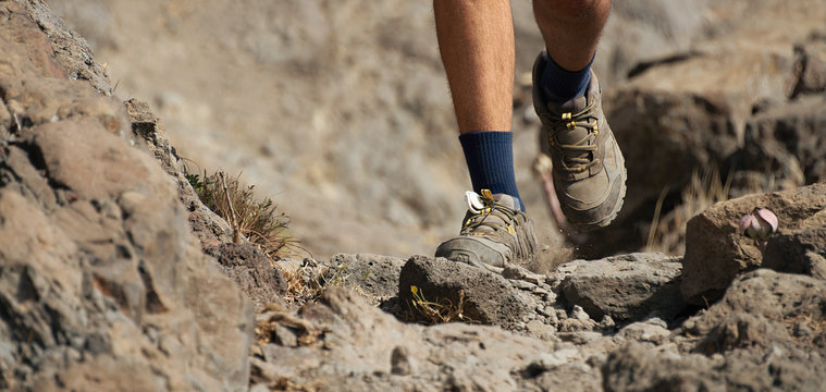 Athlete trail running in the mountains on rocky terrain, sports shoes detail