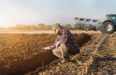 Young farmer examing  planted wheat while tractor is plowing fields