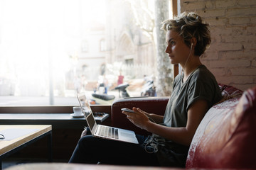 Young business woman is typing emails by a laptop while sitting in a modern coffee shop. Freelancer...