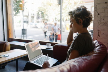 View from aside photo of a young woman with blonde hair wearing t-shirt looking at the blank white display of a modern laptop. Empty desktop of a portable computer for your logo or design.