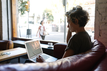 View from aside photo of a young woman with blonde hair wearing t-shirt looking at the blank white display of a modern portable computer. Empty desktop of a laptop for your logo or design.