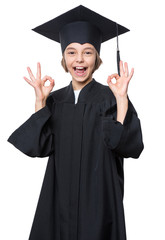 Graduate little happy girl student in black graduation gown with hat showing ok gesture - isolated on white background. Child back to school and educational concept.