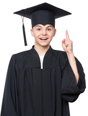 Portrait of graduate teen boy student in black graduation gown with hat has idea, pointing with finger up - isolated on white background. Child back to school and educational concept.